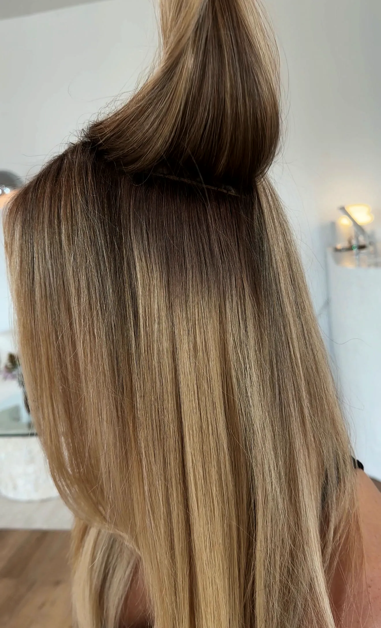 The top section lifted to show an extension weft row under long, blended hair