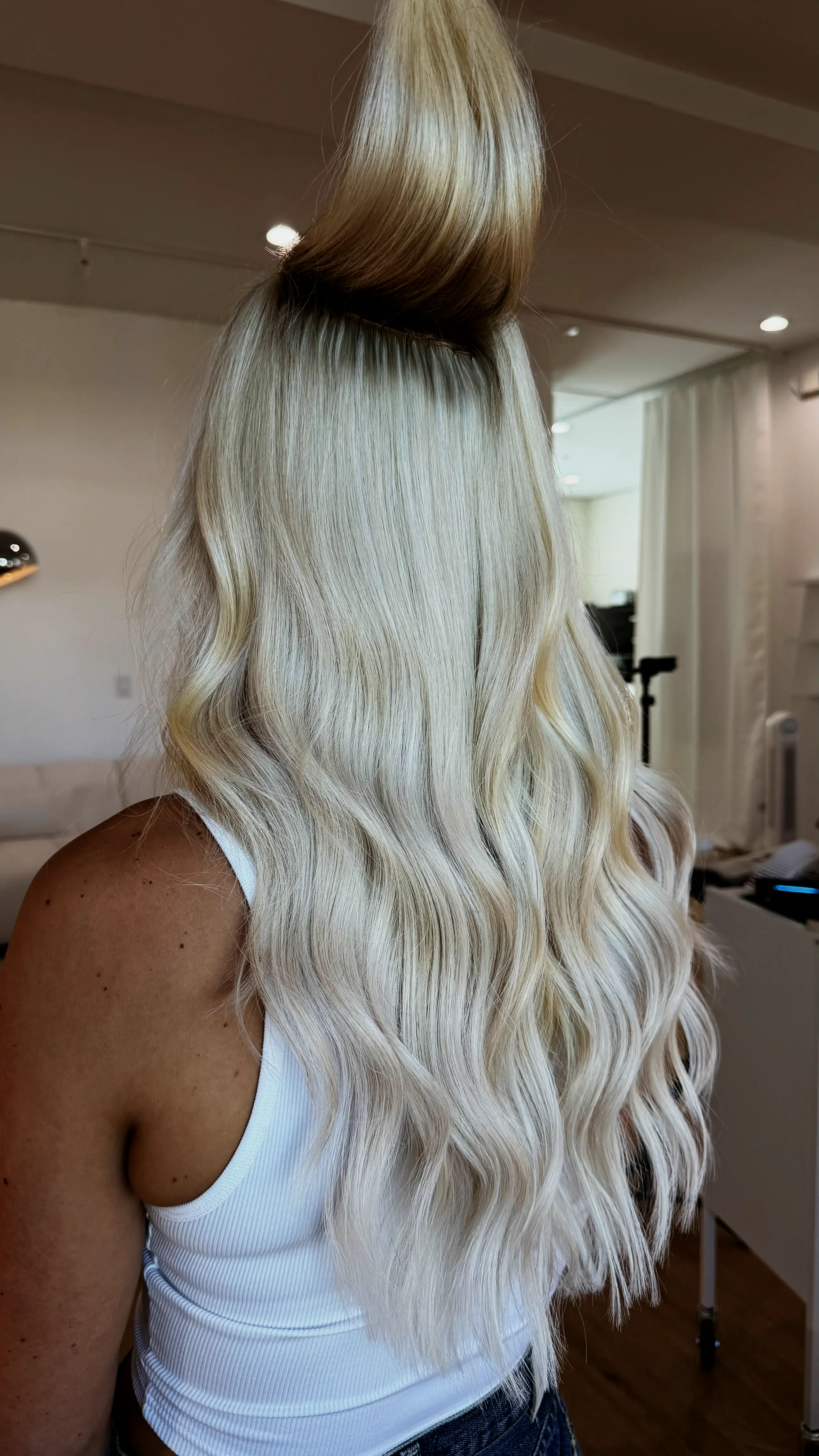 Long platinum blonde waves from behind, in a white tank top in the salon