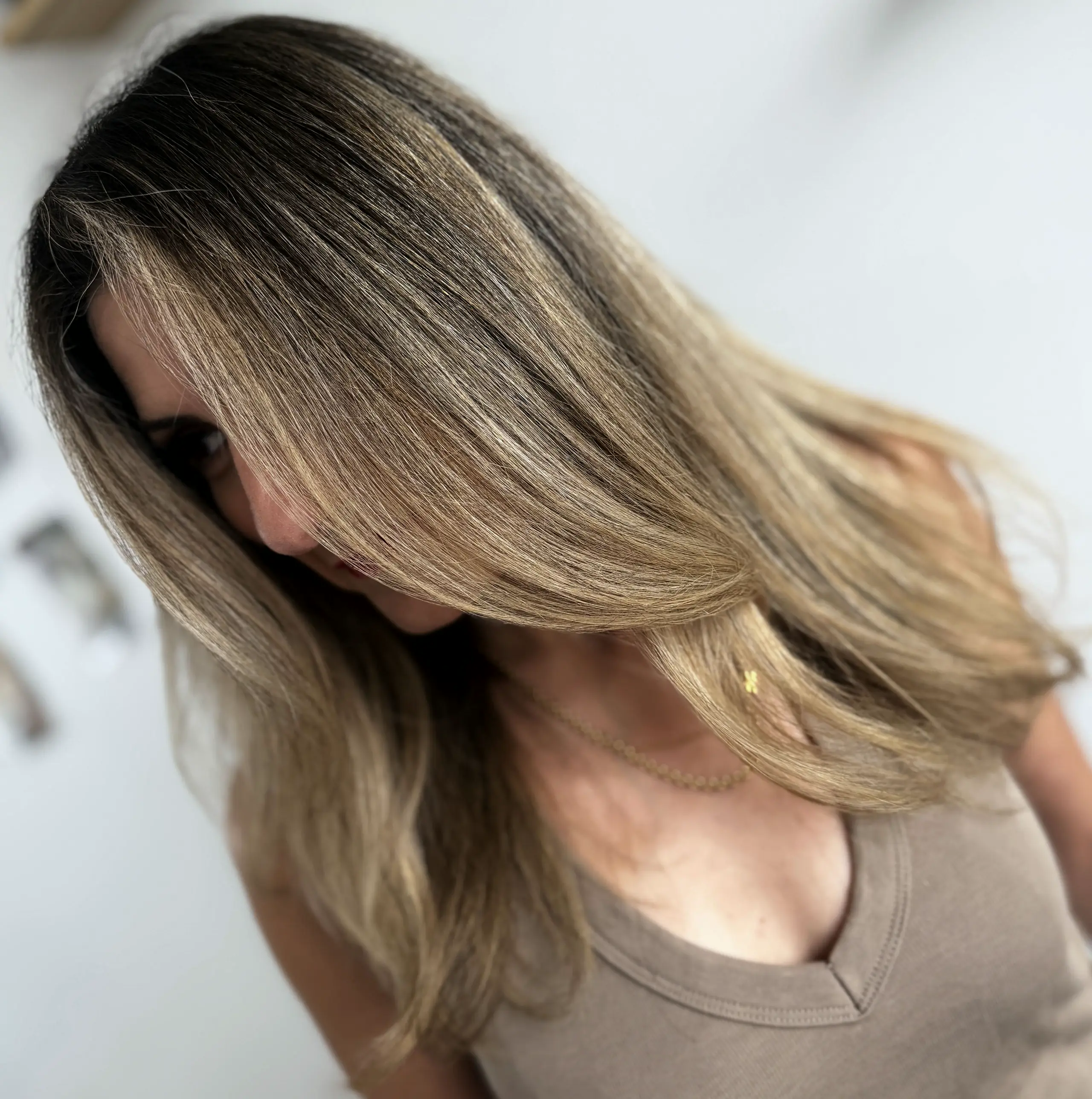 Warm bronde with bright face-framing pieces, in soft window light