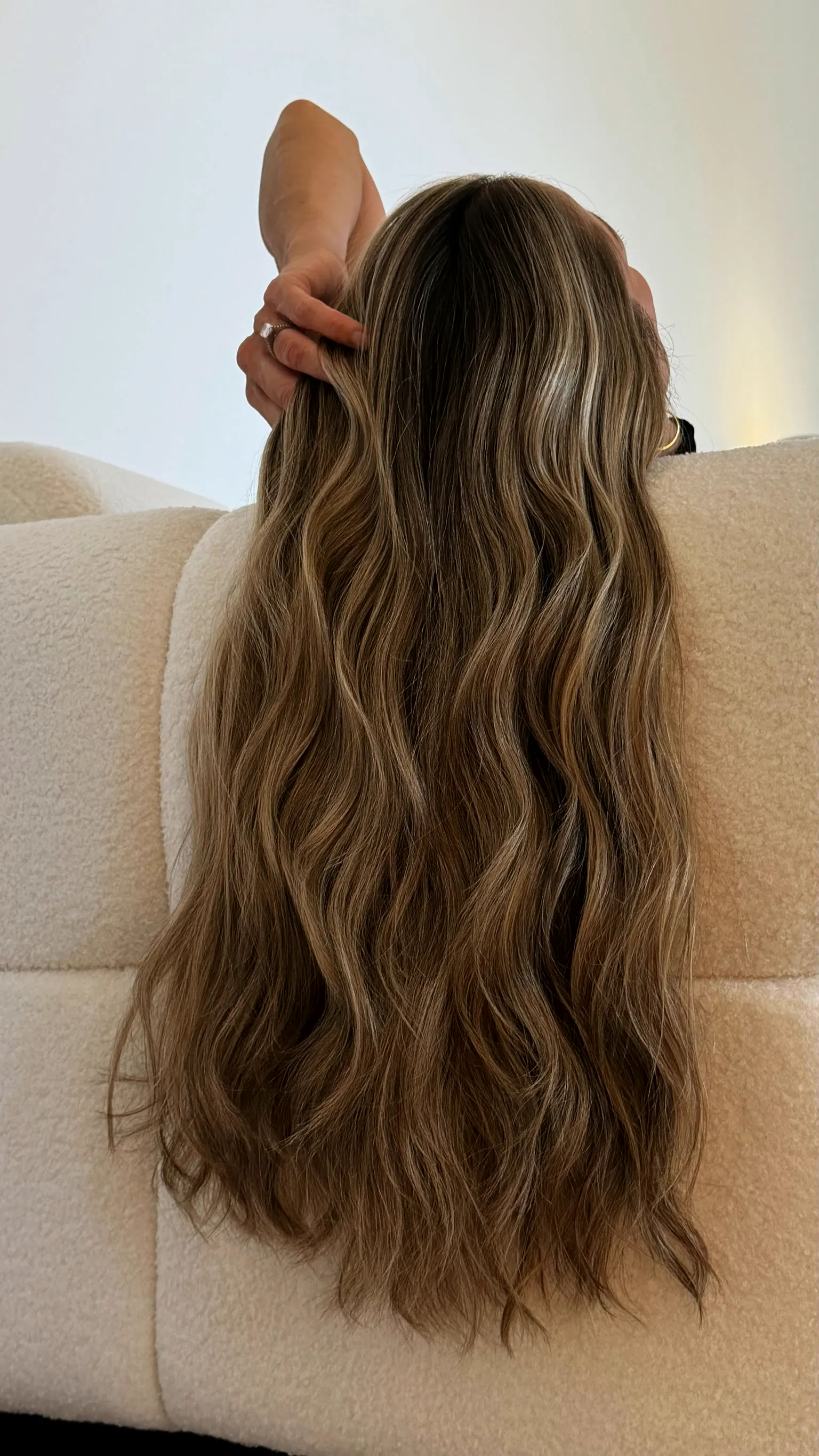 Long bronde balayage waves from behind, on a boucle sofa